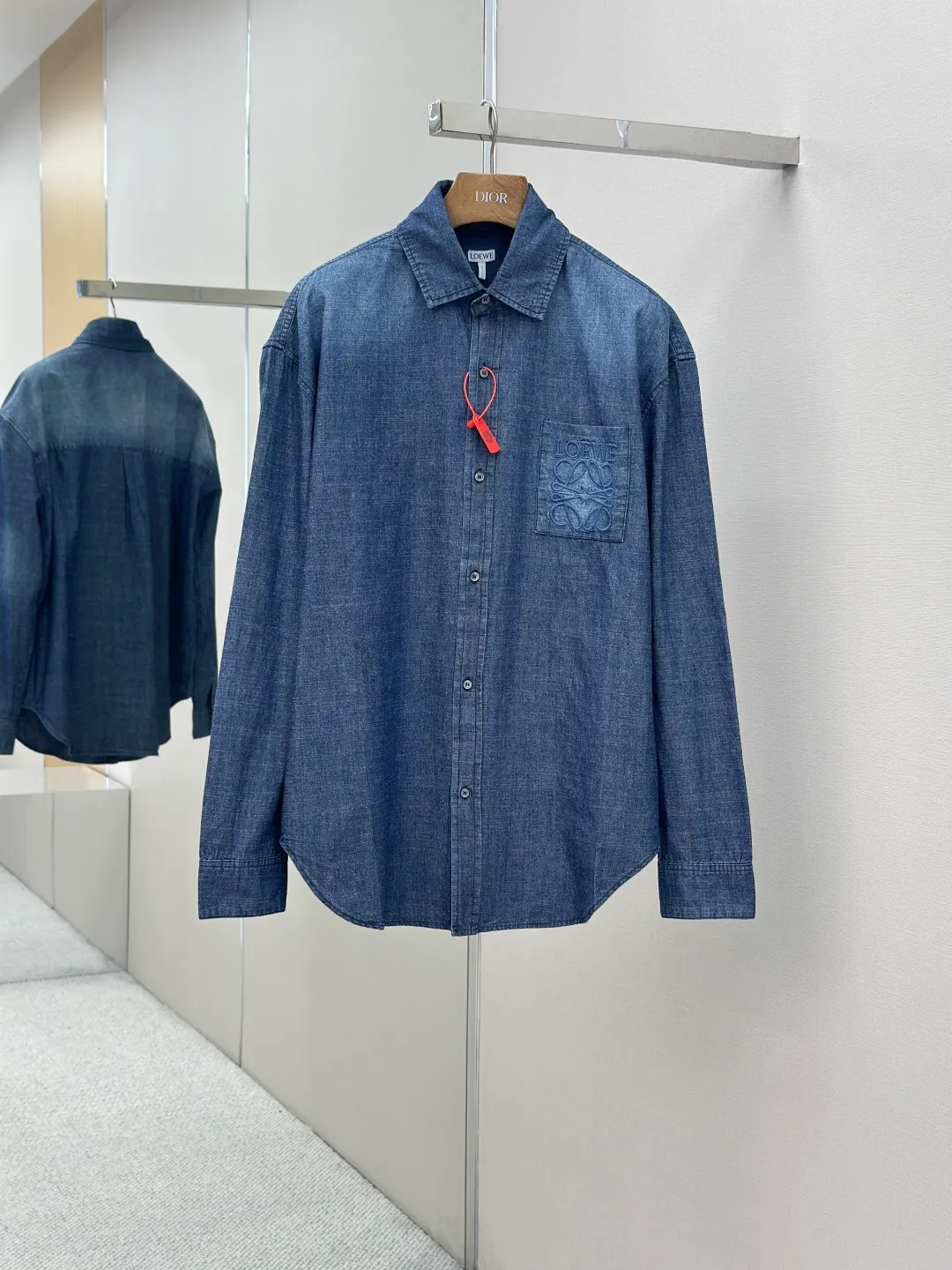 P430 Loewe Anagram Gradient Embroidered Pocket Shirt Made of custom-made high-quality cotton chambray fabric, with a unique washed gradient blue as the main tone, from dark to light and from thick to light. The chest patch pocket is decorated with Loewe Anagram embroidery as its soul, engraved with LOEWE-style casual elegance, and the natural and smooth lines show the casualness.  Imported embroidery machines are used, and advanced computer control systems and precision mechanical components are used to realize Loewe embroidery operations.  The gradient dynamic spray dyeing process uses specialized spray dyeing equipment to accurately spray dye onto the surface of the fabric in the form of mist (by accurately controlling the different dimensions of the spray of the spray dyeing equipment, combined with the movement speed and direction during the dyeing process) to present a smooth and natural transition effect of color. The butterfly rhyme pinch pleating body dart technology is inspired by the beautiful shape of butterflies, and uses precise pinch pleating techniques to create a flexible pleat effect like butterfly wings on the garment, making the garment fit more closely to the body.  size:44.46.48.50